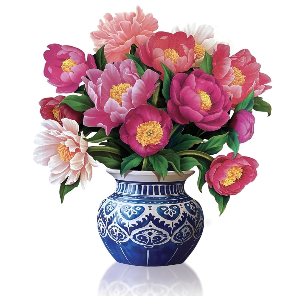 A decorative blue and white vase holds a vibrant bouquet of pink, red, and white peonies with lush green leaves, reminiscent of easy flower paper crafts, creating a striking contrast against the white background.